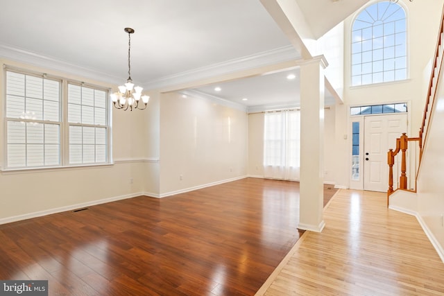 interior space featuring ornate columns, light hardwood / wood-style floors, ornamental molding, and a notable chandelier