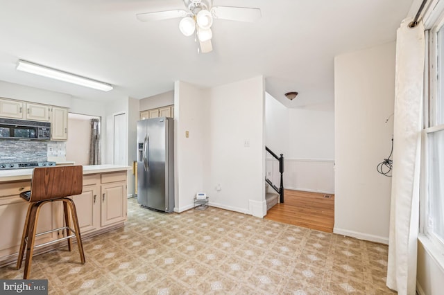 kitchen with a breakfast bar, ceiling fan, tasteful backsplash, cream cabinetry, and stainless steel fridge with ice dispenser