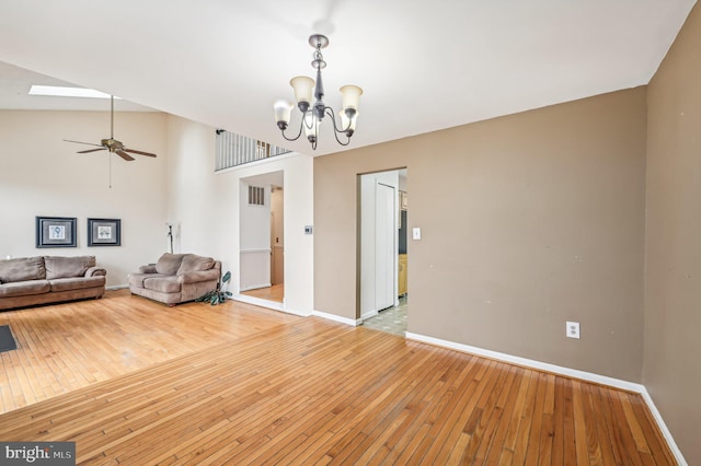 unfurnished living room featuring a skylight, light hardwood / wood-style flooring, high vaulted ceiling, and ceiling fan with notable chandelier