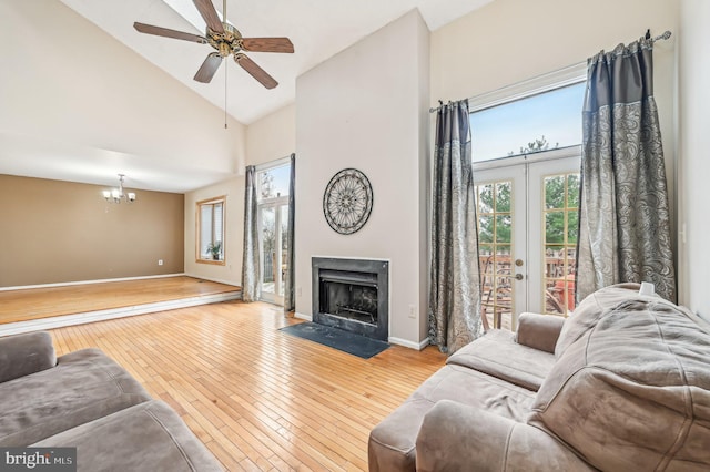 living room with french doors, ceiling fan with notable chandelier, high vaulted ceiling, and light hardwood / wood-style flooring