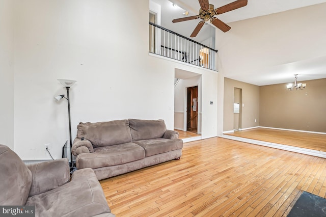 living room featuring ceiling fan with notable chandelier, light wood-type flooring, and a high ceiling