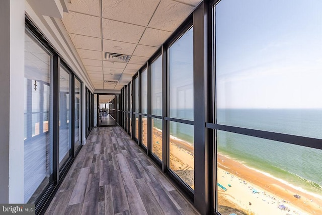 hallway with a paneled ceiling, expansive windows, a view of the beach, a water view, and dark hardwood / wood-style floors