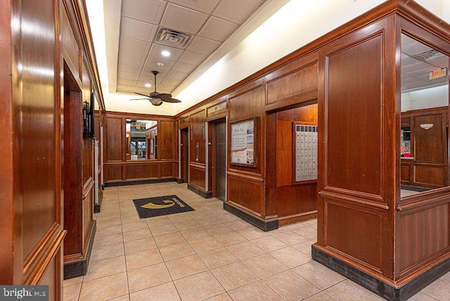 corridor with a raised ceiling, wooden walls, and light tile patterned flooring