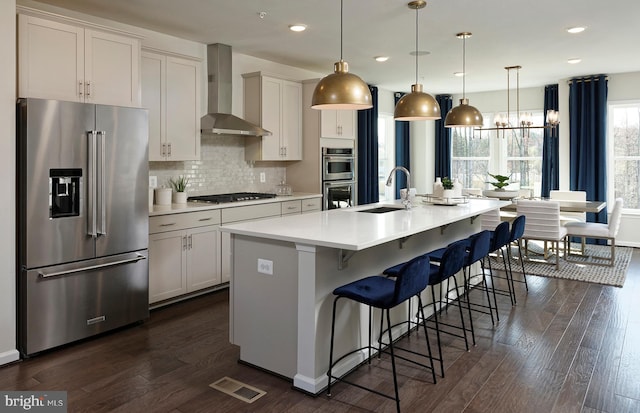 kitchen with dark wood-type flooring, hanging light fixtures, sink, a kitchen island with sink, and appliances with stainless steel finishes