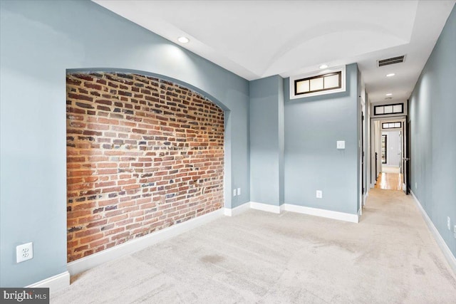 carpeted spare room featuring brick wall