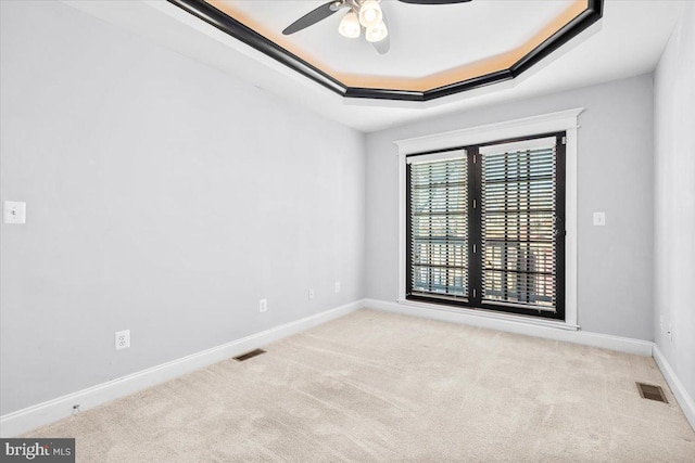 carpeted spare room with a raised ceiling and ceiling fan