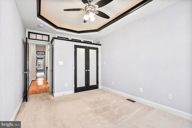 unfurnished bedroom featuring light carpet, french doors, a tray ceiling, and ceiling fan