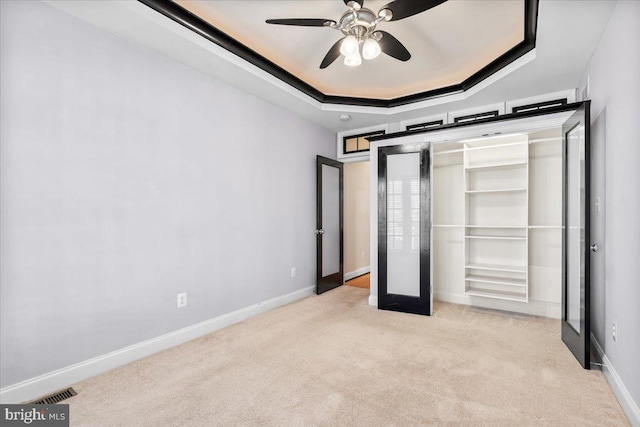 unfurnished bedroom featuring light carpet, french doors, a tray ceiling, ceiling fan, and a closet