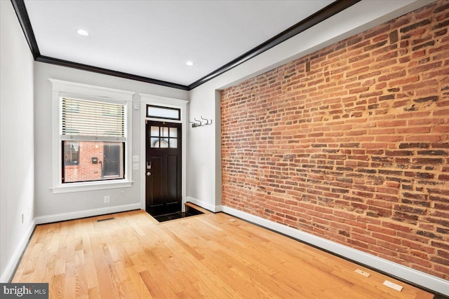 foyer entrance with ornamental molding, baseboards, light wood finished floors, and brick wall