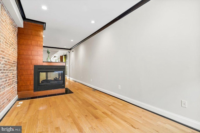 unfurnished living room with a multi sided fireplace, hardwood / wood-style flooring, ornamental molding, and brick wall