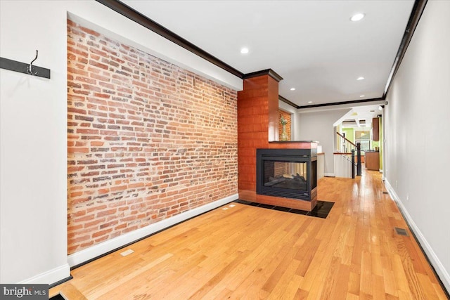 unfurnished living room with a multi sided fireplace, light wood-type flooring, crown molding, and brick wall