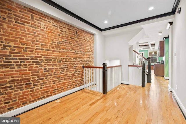 hall featuring crown molding, brick wall, and light wood-type flooring