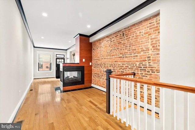 hall with light hardwood / wood-style flooring, ornamental molding, and brick wall