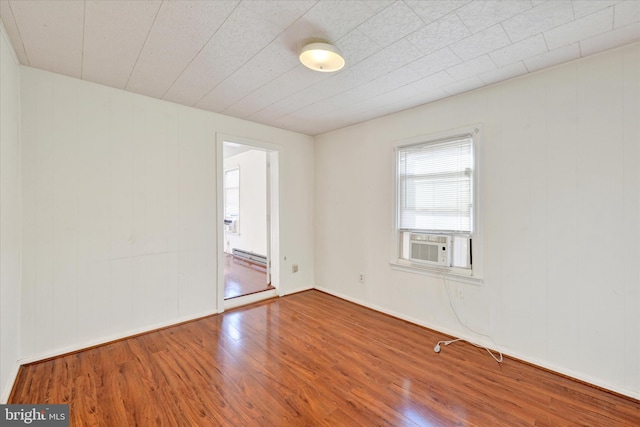 empty room with wood-type flooring, cooling unit, and baseboard heating