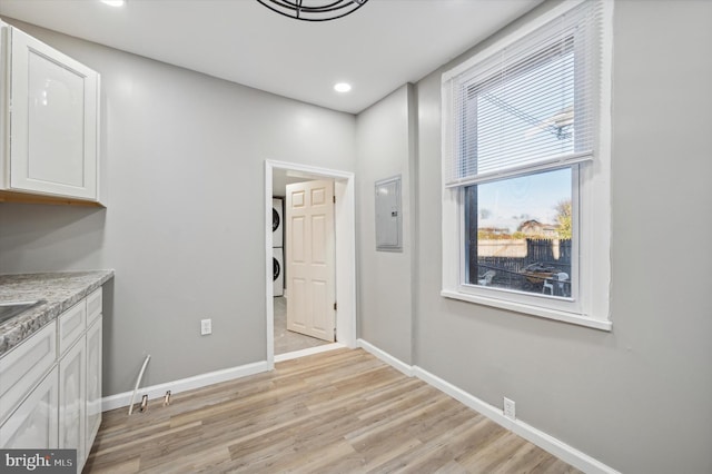 interior space with electric panel, stacked washer and dryer, and light hardwood / wood-style floors