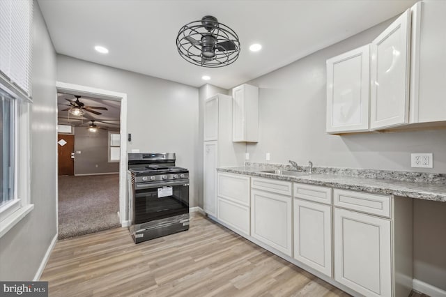 kitchen with white cabinetry, stainless steel gas range, light stone countertops, sink, and light hardwood / wood-style flooring