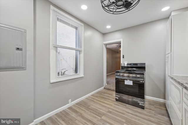 kitchen with electric panel, stainless steel range with gas cooktop, ceiling fan, white cabinetry, and light hardwood / wood-style flooring