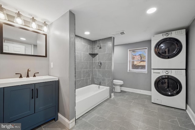 full bathroom featuring stacked washing maching and dryer, tile patterned floors, vanity, tiled shower / bath combo, and toilet