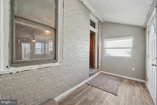 interior space featuring ceiling fan, wood-type flooring, brick wall, and lofted ceiling