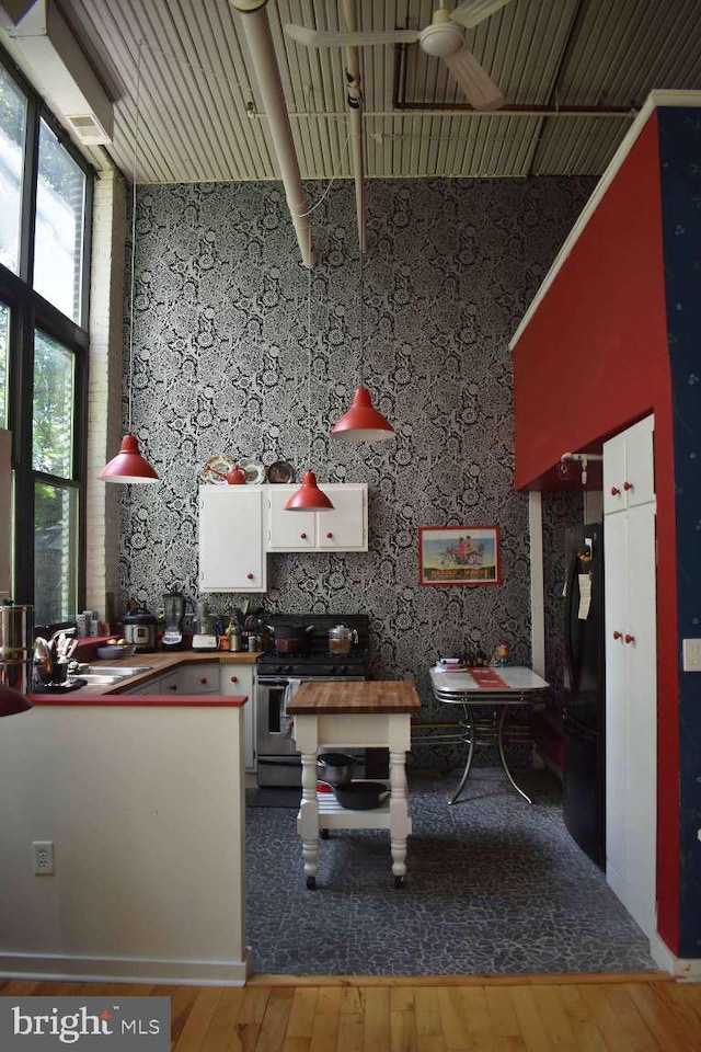 interior space featuring black fridge, stainless steel range with electric cooktop, a towering ceiling, white cabinetry, and hardwood / wood-style flooring