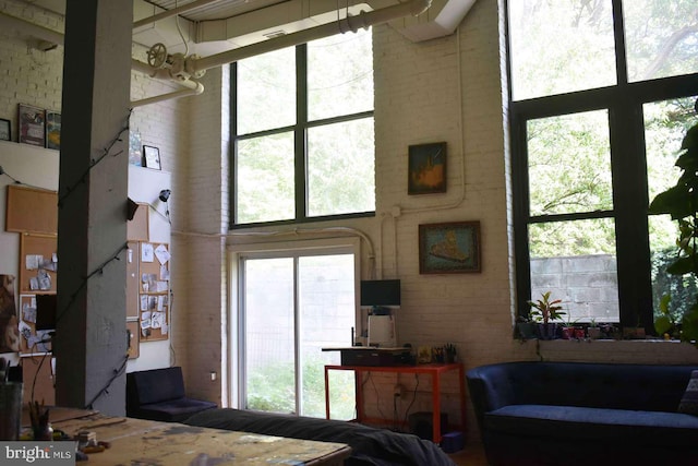 living room featuring a wealth of natural light, a high ceiling, and brick wall