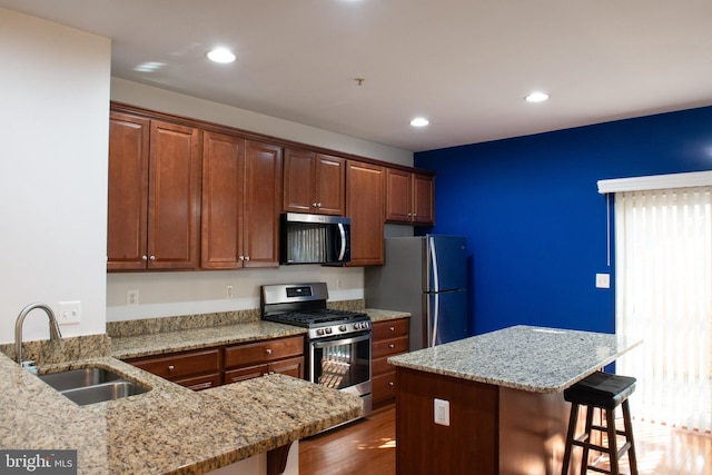 kitchen with a breakfast bar, dark wood-type flooring, sink, light stone counters, and stainless steel appliances