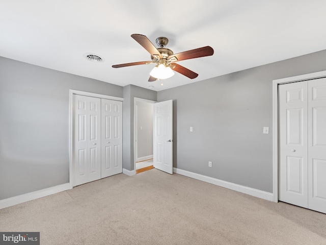 unfurnished bedroom with light colored carpet, ceiling fan, and multiple closets