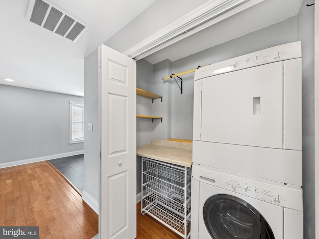 clothes washing area with stacked washer / dryer and dark wood-type flooring