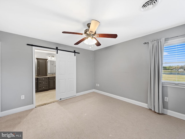 unfurnished bedroom with ceiling fan, a barn door, light colored carpet, and connected bathroom