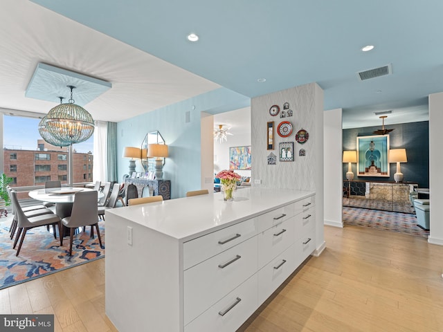 kitchen with hanging light fixtures, a kitchen island, a notable chandelier, light hardwood / wood-style floors, and white cabinetry