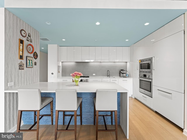 kitchen featuring white cabinetry, kitchen peninsula, a breakfast bar area, appliances with stainless steel finishes, and light wood-type flooring