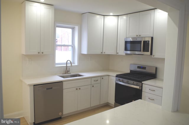 kitchen featuring sink, appliances with stainless steel finishes, white cabinetry, tasteful backsplash, and light stone countertops