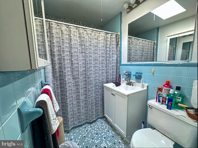 bathroom featuring a skylight, vanity, tile walls, tile patterned flooring, and toilet