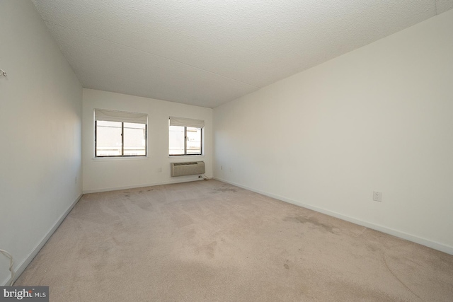 unfurnished room with an AC wall unit, light colored carpet, and a textured ceiling