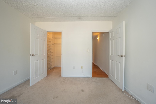 unfurnished bedroom featuring a textured ceiling, light colored carpet, a spacious closet, and a closet