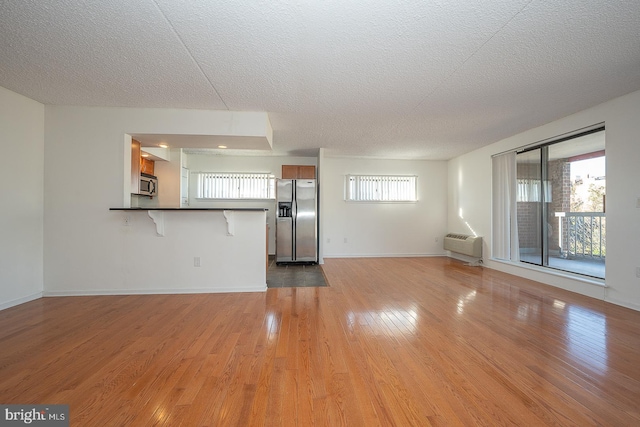 unfurnished living room with a wall mounted air conditioner, light wood-type flooring, and a textured ceiling