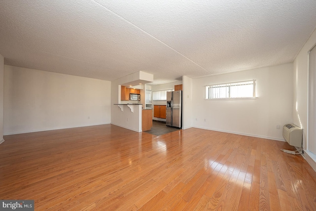 unfurnished living room with a textured ceiling, light hardwood / wood-style floors, and a wall unit AC