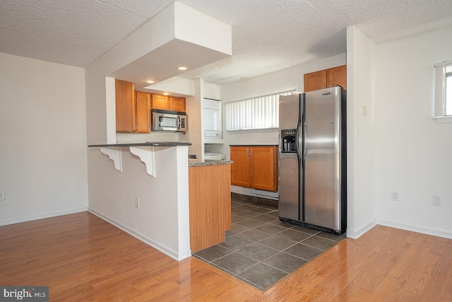 kitchen with a kitchen breakfast bar, dark hardwood / wood-style floors, appliances with stainless steel finishes, a healthy amount of sunlight, and kitchen peninsula