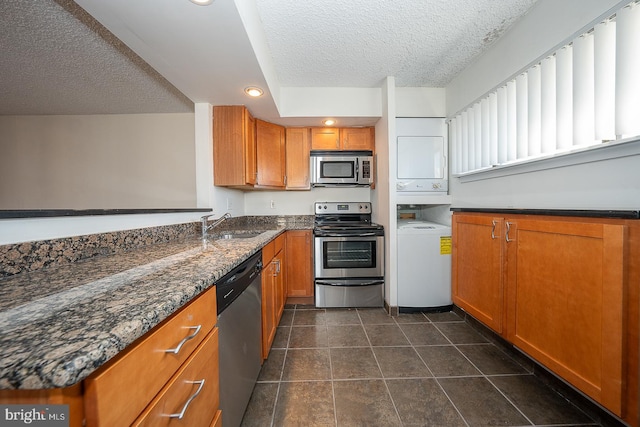 kitchen with dark stone countertops, dark tile patterned floors, a textured ceiling, stacked washer / drying machine, and stainless steel appliances