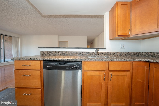 kitchen with dark wood-type flooring, dark stone counters, sink, stainless steel dishwasher, and a textured ceiling