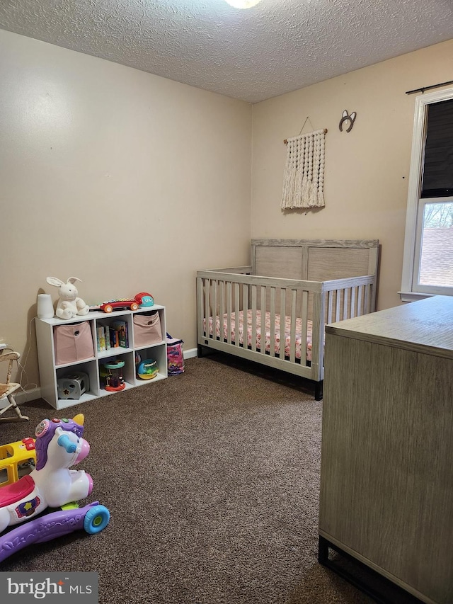 bedroom featuring a nursery area, a textured ceiling, and dark carpet