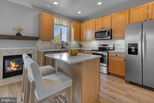 kitchen featuring appliances with stainless steel finishes, tasteful backsplash, a center island, light wood-type flooring, and a sink