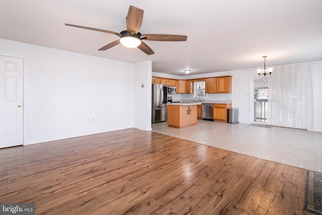 unfurnished living room featuring ceiling fan with notable chandelier, light wood-type flooring, and sink