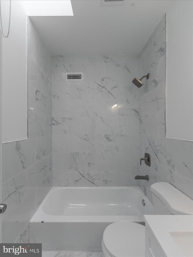 full bathroom with tiled shower / bath, vanity, toilet, and tile walls