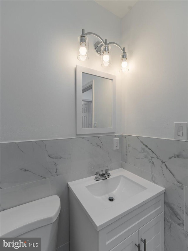 bathroom featuring vanity, toilet, and tile walls