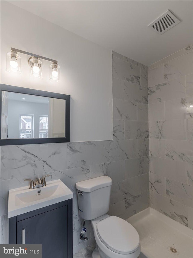 bathroom with a tile shower, vanity, tile walls, and toilet