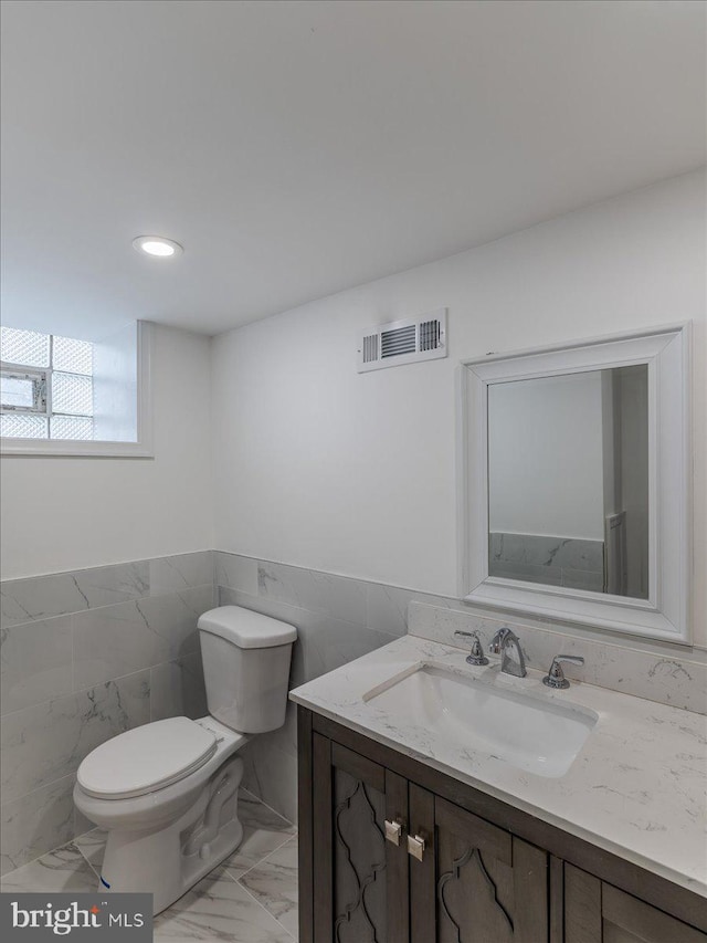 bathroom with vanity, toilet, and tile walls