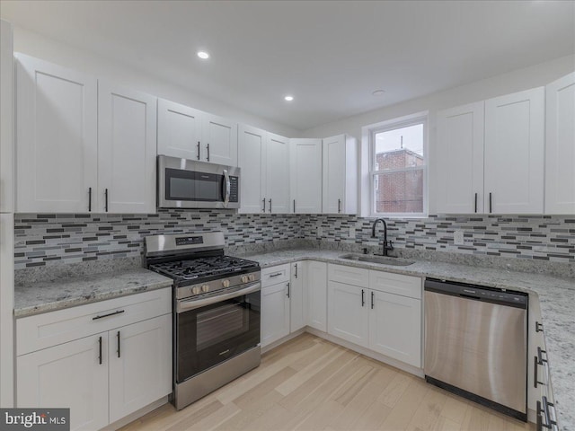 kitchen with decorative backsplash, appliances with stainless steel finishes, sink, white cabinets, and light hardwood / wood-style floors