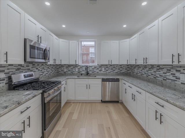 kitchen featuring sink, light hardwood / wood-style flooring, appliances with stainless steel finishes, tasteful backsplash, and white cabinetry