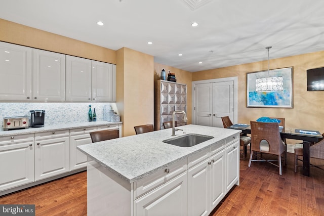 kitchen with sink, hanging light fixtures, a kitchen island with sink, white cabinets, and hardwood / wood-style flooring